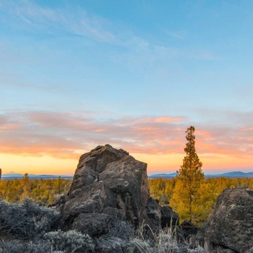 A hiker perches on a lava rock pillar to admire sunset in the Badlands Wilderness