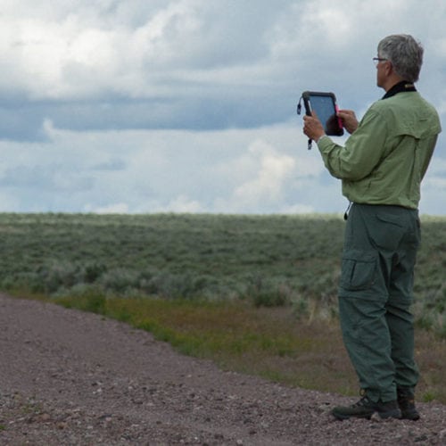 A lone volunteer with an iPad takes photos in Oregon's high desert backcountry.