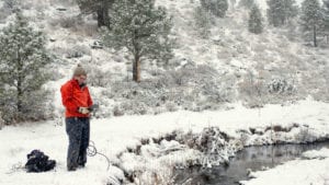 a volunteer wearing a read jacket stands out on snowy day along a desert creek